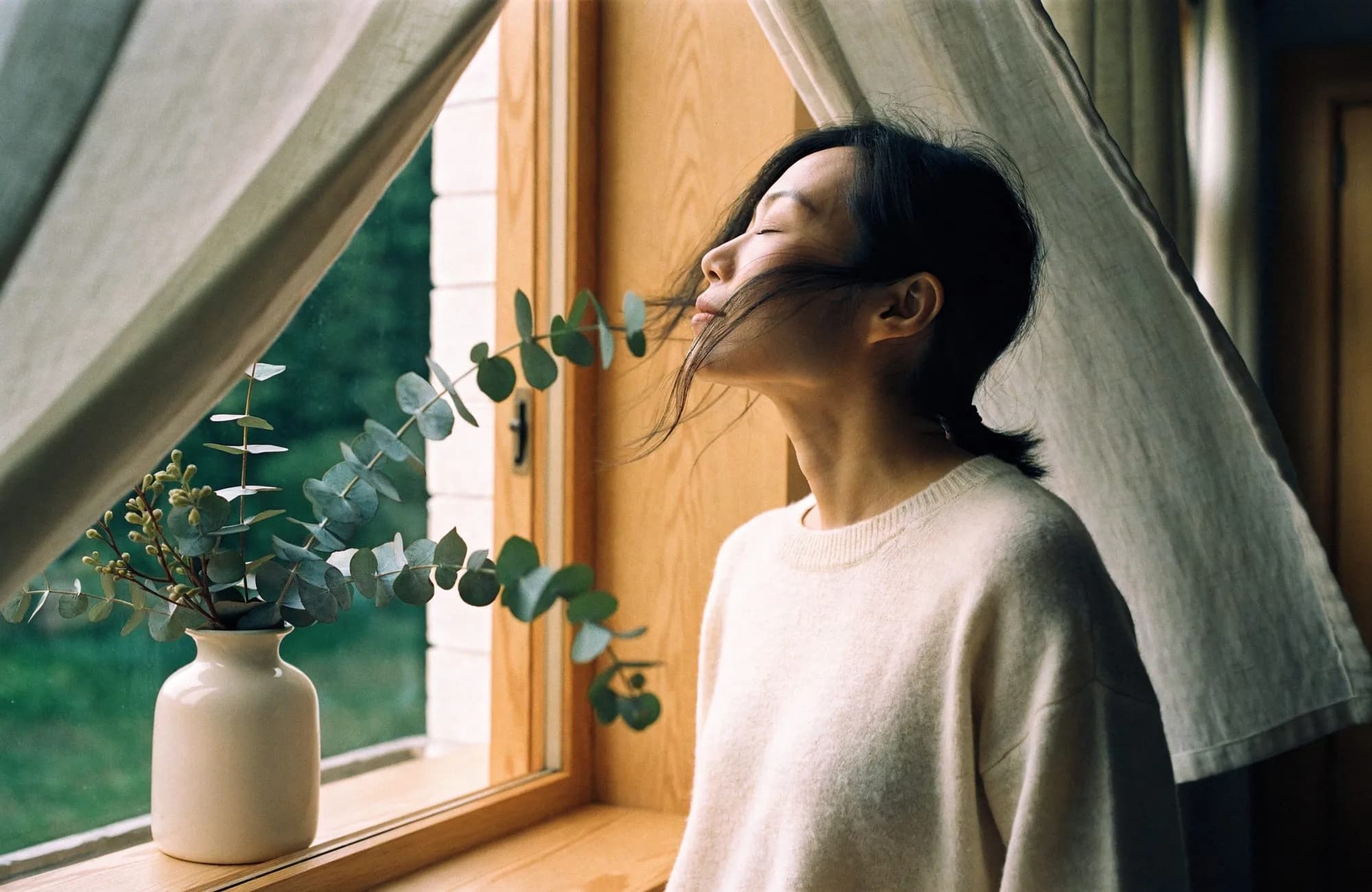 A woman breathing in fresh air by an open window, eucalyptus on the sill