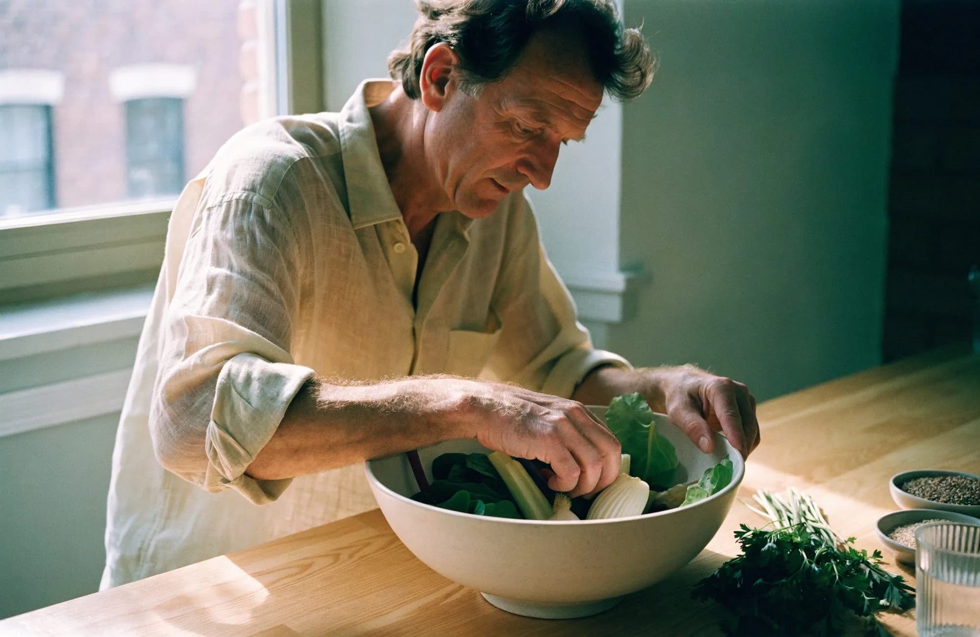 A man preparing fresh vegetables and greens in a ceramic bowl